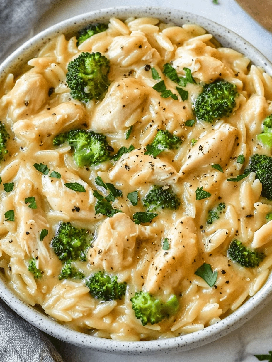 cheesy-orzo-chicken-broccoli-top-view-golden-bowl Top-down shot of a white bowl filled with cheesy chicken broccoli orzo pasta, garnished with parsley and black pepper.