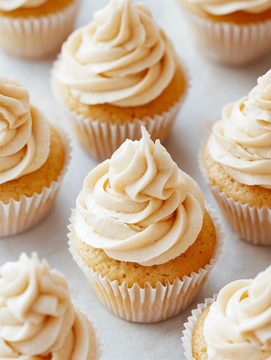 Gluten-free cupcakes topped with piped cinnamon frosting, arranged on a light surface in white paper liners.
